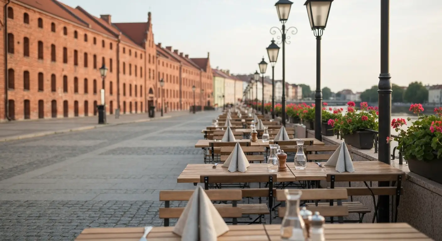 Pusty taras restauracji z drewnianymi stolikami na brukowanej uliczce w centrum Bydgoszczy, w tle ceglane spichrze nad B