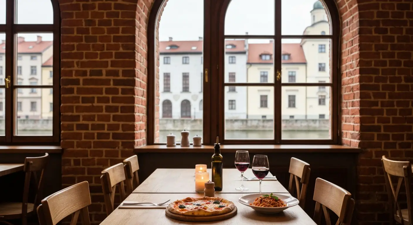 Stolik we wloskiej restauracji w Bydgoszczy z pizza i makaronem, w tle okno z widokiem na kamienice i spichrze nad Brda