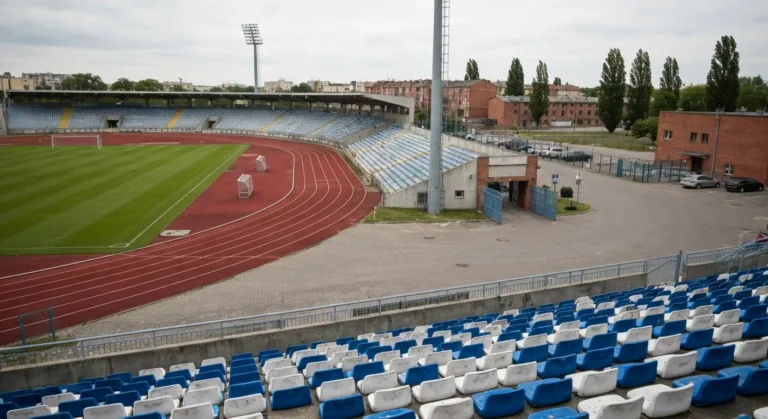 Puste trybuny bydgoskiego stadionu z bieznia i boiskiem, w tle maszty oswietleniowe i parking
