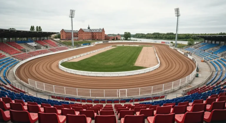 Pusty stadion zuzlowy w Bydgoszczy - owalny tor, bandy i rzedy kolorowych krzeselek, w tle zielen doliny Brdy